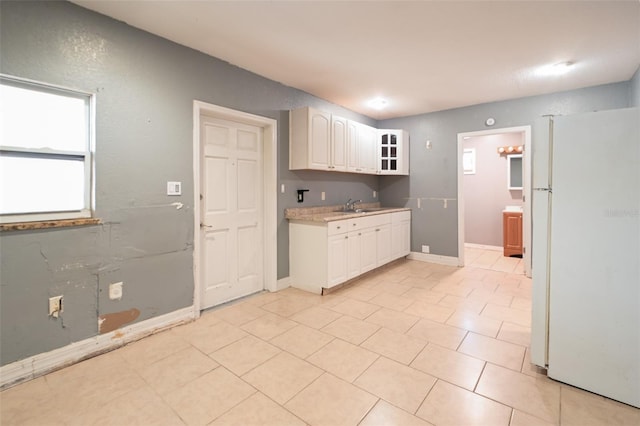 kitchen featuring light countertops, glass insert cabinets, freestanding refrigerator, white cabinetry, and a sink