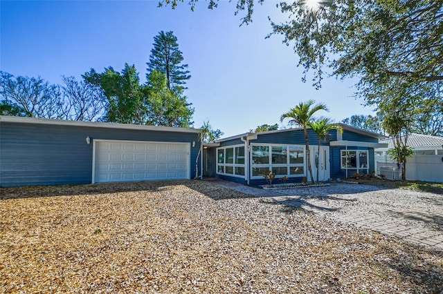 mid-century modern home with an attached garage, gravel driveway, fence, and a sunroom