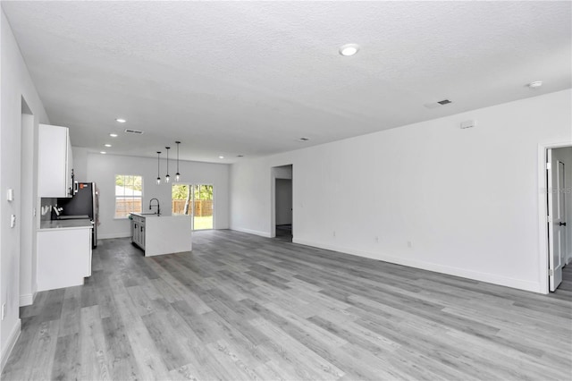unfurnished living room featuring a sink, a textured ceiling, light wood finished floors, and baseboards