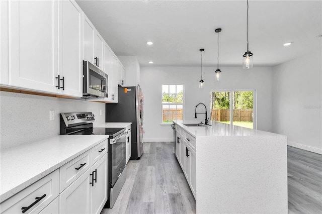 kitchen with white cabinets, appliances with stainless steel finishes, a sink, light wood-style floors, and an island with sink