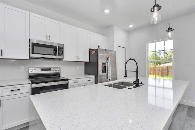 kitchen featuring an island with sink, white cabinetry, a sink, appliances with stainless steel finishes, and hanging light fixtures