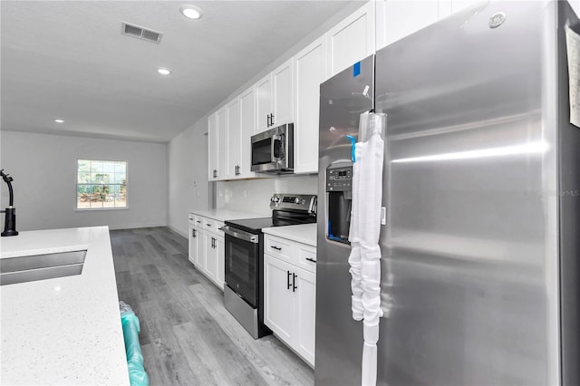 kitchen featuring visible vents, light wood-style flooring, white cabinets, and stainless steel appliances