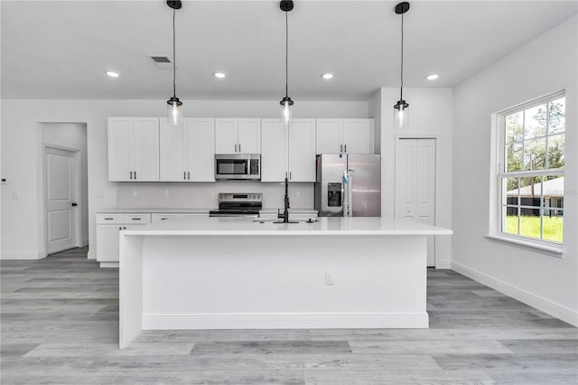 kitchen featuring stainless steel appliances, baseboards, a center island with sink, and a sink