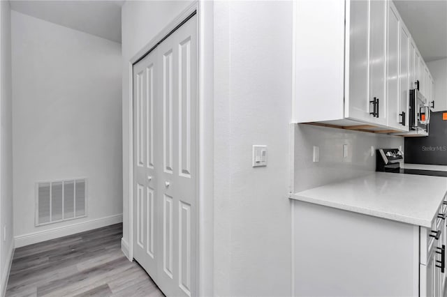 kitchen featuring white cabinets, light wood-style flooring, baseboards, stainless steel microwave, and visible vents
