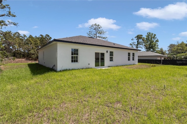 rear view of house featuring a lawn, fence, and stucco siding