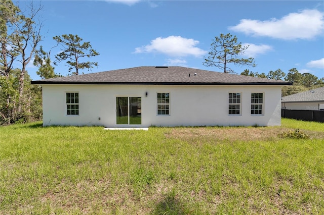 rear view of property with roof with shingles, stucco siding, a yard, and fence