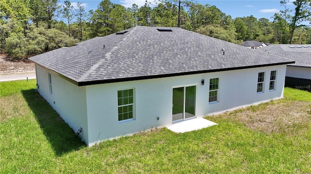rear view of property with a shingled roof, stucco siding, and a yard