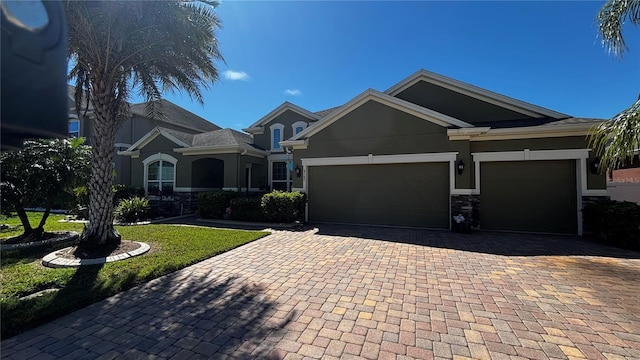 view of front of home featuring a garage, decorative driveway, stone siding, and stucco siding