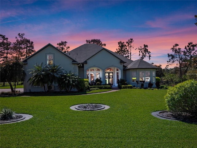 view of front of home with french doors, a lawn, and stucco siding