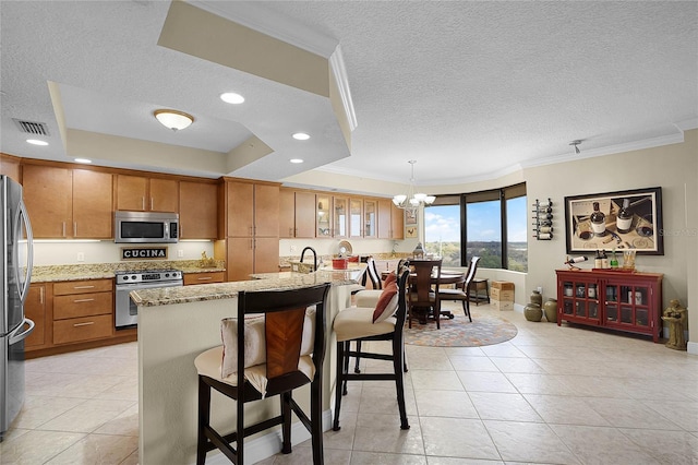 kitchen featuring a tray ceiling, stainless steel appliances, visible vents, brown cabinetry, and light stone countertops