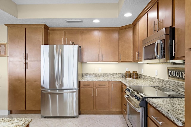 kitchen featuring light tile patterned floors, light stone counters, visible vents, appliances with stainless steel finishes, and brown cabinets