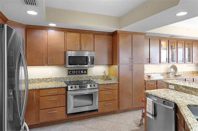 kitchen with light tile patterned floors, visible vents, appliances with stainless steel finishes, brown cabinets, and light stone counters