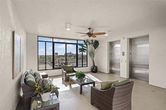 living area featuring a ceiling fan, elevator, a textured wall, and a textured ceiling