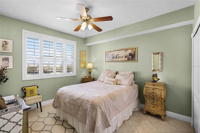 bedroom featuring a textured ceiling, ceiling fan, light tile patterned floors, and baseboards