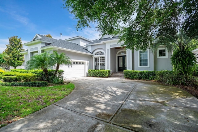 view of front of property with stucco siding, driveway, a garage, and roof with shingles