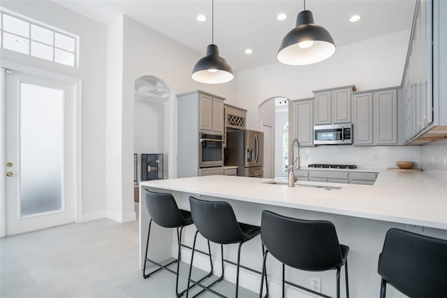 kitchen with gray cabinetry, a peninsula, arched walkways, stainless steel appliances, and a sink