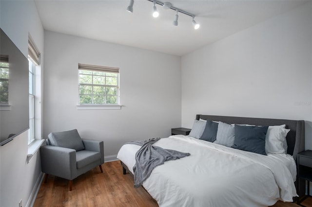 bedroom with rail lighting, baseboards, and wood finished floors