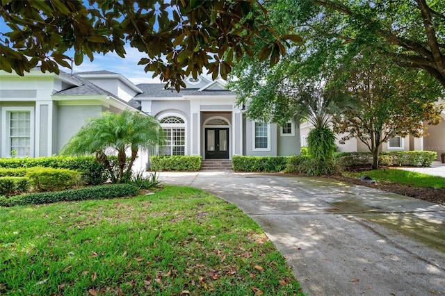 view of front of house featuring concrete driveway, french doors, a front lawn, and stucco siding