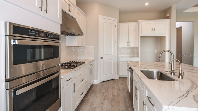 kitchen with appliances with stainless steel finishes, white cabinets, a sink, and under cabinet range hood