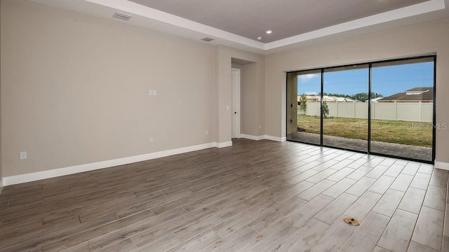 unfurnished room with a tray ceiling, wood finished floors, visible vents, and baseboards