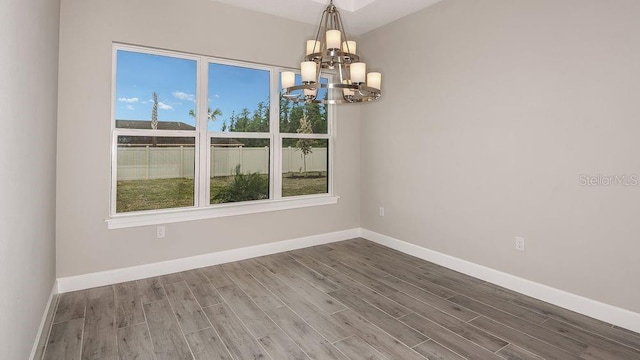 unfurnished room featuring baseboards, a notable chandelier, and wood finished floors