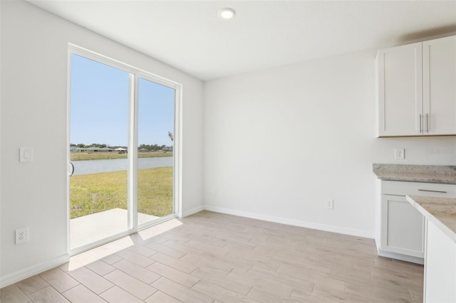 kitchen featuring white cabinets, baseboards, light wood-type flooring, and a water view