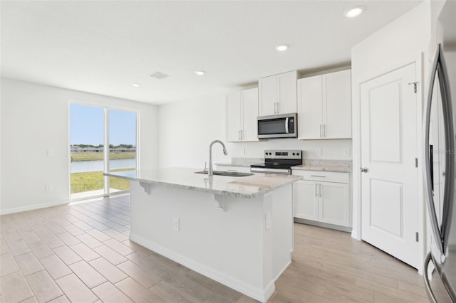 kitchen featuring stainless steel appliances, visible vents, a sink, baseboards, and a kitchen island with sink