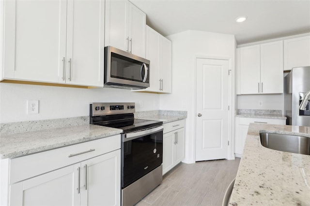 kitchen featuring white cabinets, light wood-style floors, appliances with stainless steel finishes, and light stone counters
