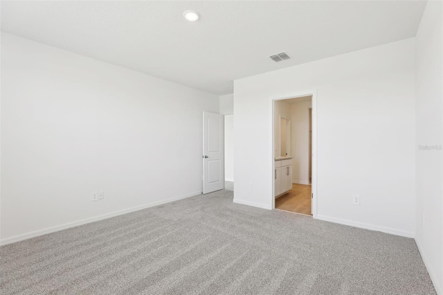 unfurnished bedroom featuring recessed lighting, visible vents, ensuite bath, baseboards, and light colored carpet