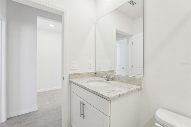 half bathroom with toilet, baseboards, visible vents, wood finished floors, and vanity
