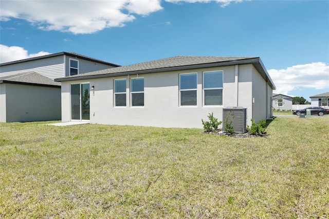 back of property featuring stucco siding, central AC unit, a yard, and a shingled roof