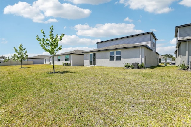 rear view of property featuring a lawn, central air condition unit, and stucco siding