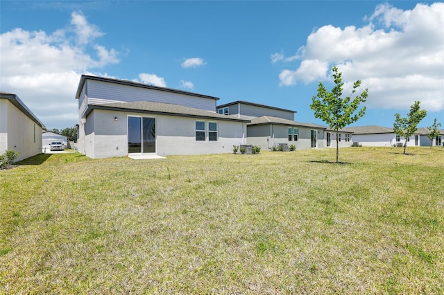 rear view of house featuring a lawn and stucco siding