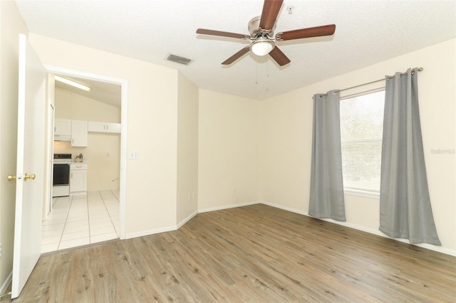 spare room with a ceiling fan, light wood-type flooring, visible vents, and a textured ceiling