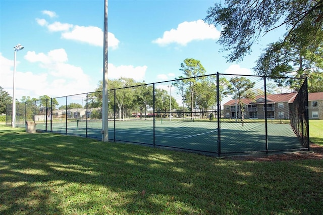 view of tennis court with a lawn and fence