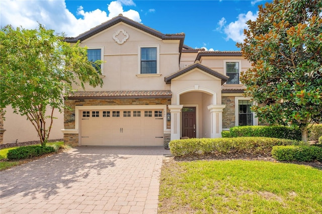 mediterranean / spanish house with decorative driveway, stucco siding, a garage, stone siding, and a tiled roof