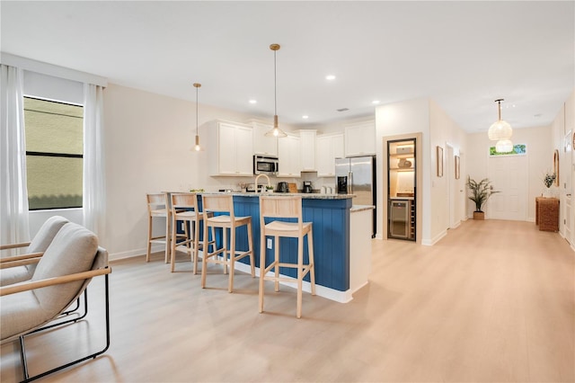 kitchen featuring light wood-style flooring, appliances with stainless steel finishes, white cabinetry, a peninsula, and a kitchen bar