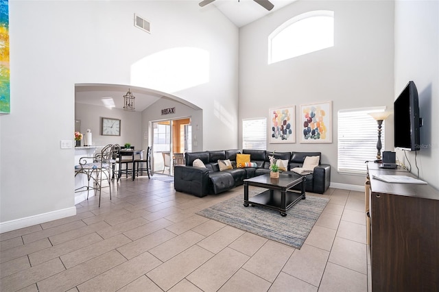 living area with visible vents, baseboards, a towering ceiling, and ceiling fan with notable chandelier