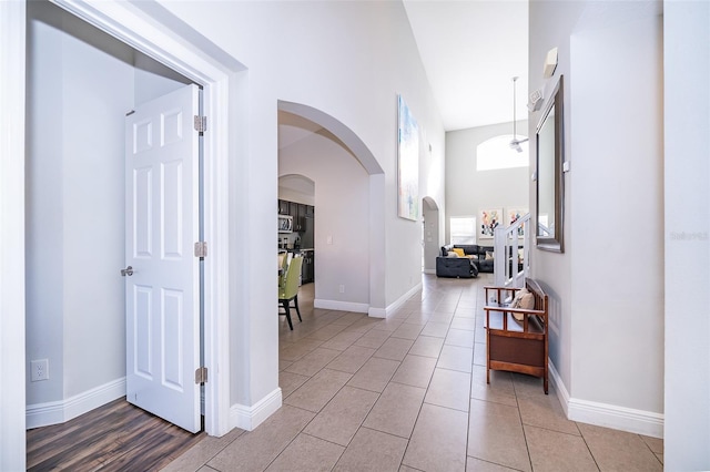 hall featuring arched walkways, light tile patterned floors, a high ceiling, and baseboards