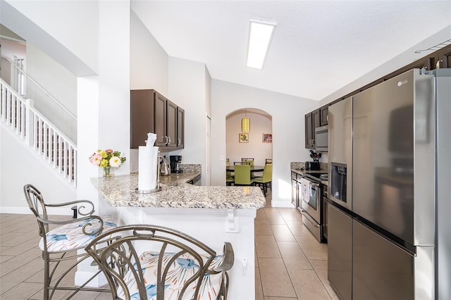 kitchen featuring stainless steel appliances, arched walkways, a peninsula, light tile patterned floors, and dark brown cabinets