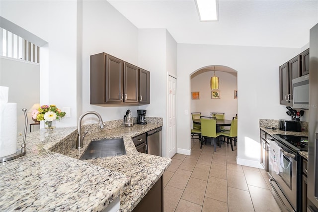 kitchen with a sink, stainless steel appliances, light stone counters, and dark brown cabinets