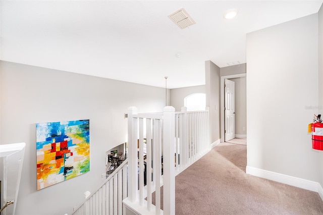 corridor with baseboards, visible vents, an upstairs landing, and light carpet