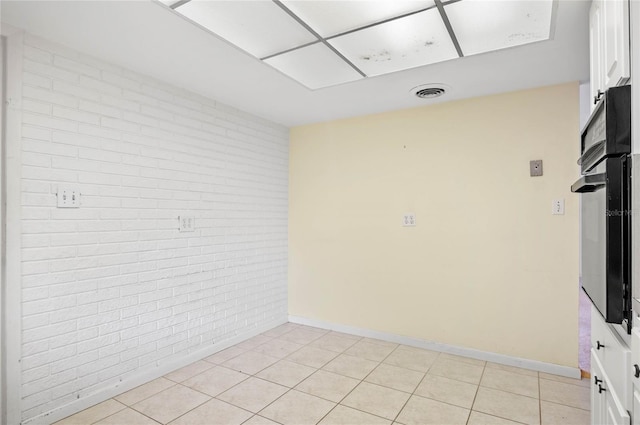 spare room featuring light tile patterned flooring, visible vents, brick wall, and baseboards