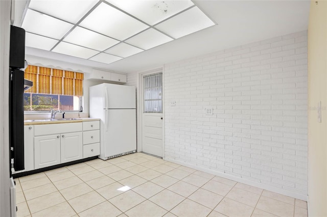 kitchen featuring a sink, white cabinetry, freestanding refrigerator, brick wall, and light countertops