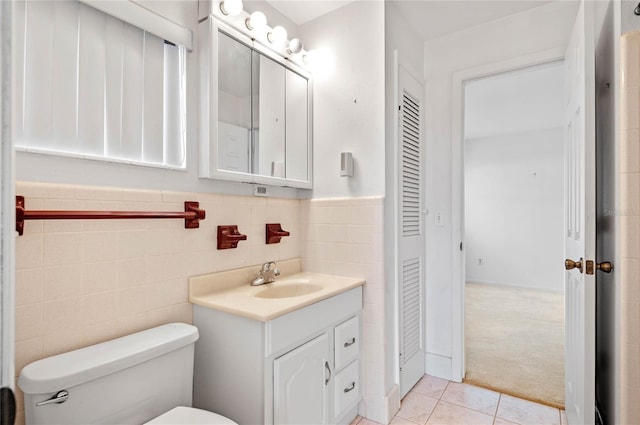 bathroom with tile patterned flooring, tile walls, a wainscoted wall, toilet, and vanity