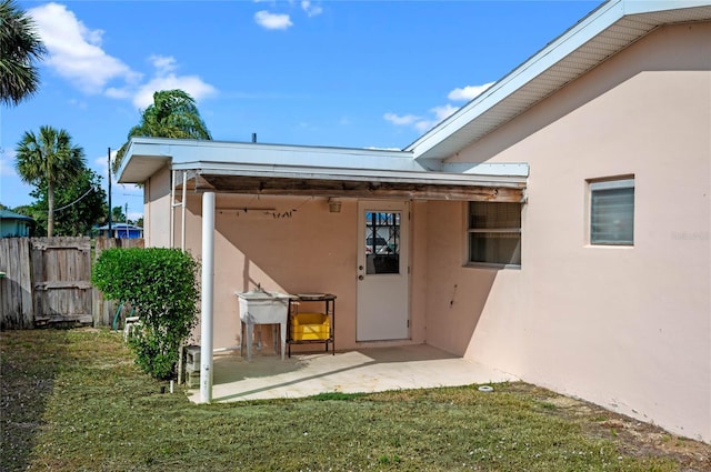 property entrance featuring stucco siding, a patio area, a yard, and fence