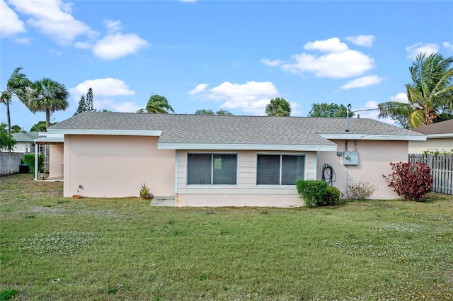 back of property featuring stucco siding, a lawn, a shingled roof, and fence