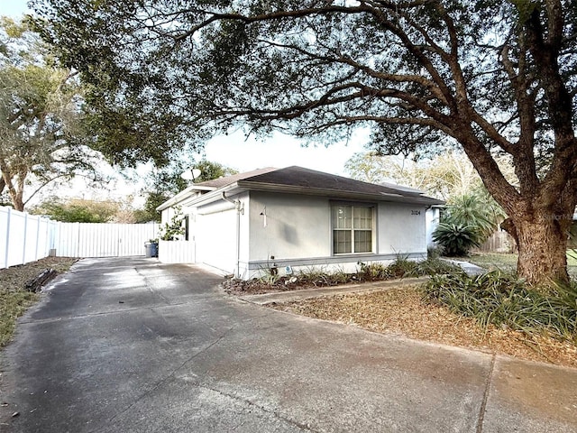 ranch-style house featuring an attached garage, fence, concrete driveway, and stucco siding