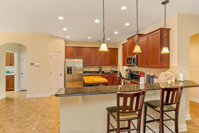 kitchen featuring a peninsula, arched walkways, stainless steel appliances, and dark stone counters