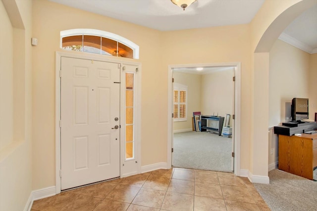 entrance foyer with arched walkways, light tile patterned floors, baseboards, and light colored carpet